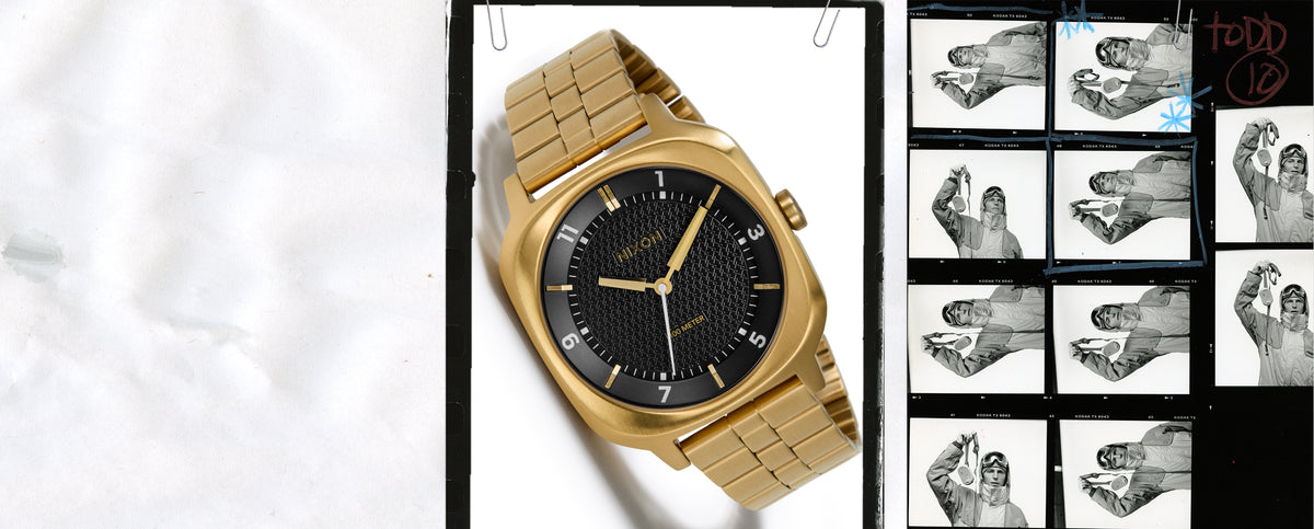 A gold-tone wristwatch with a black textured dial and matching gold-tone link bracelet, shown on a white background with a black border and a small collage of photos on the right.